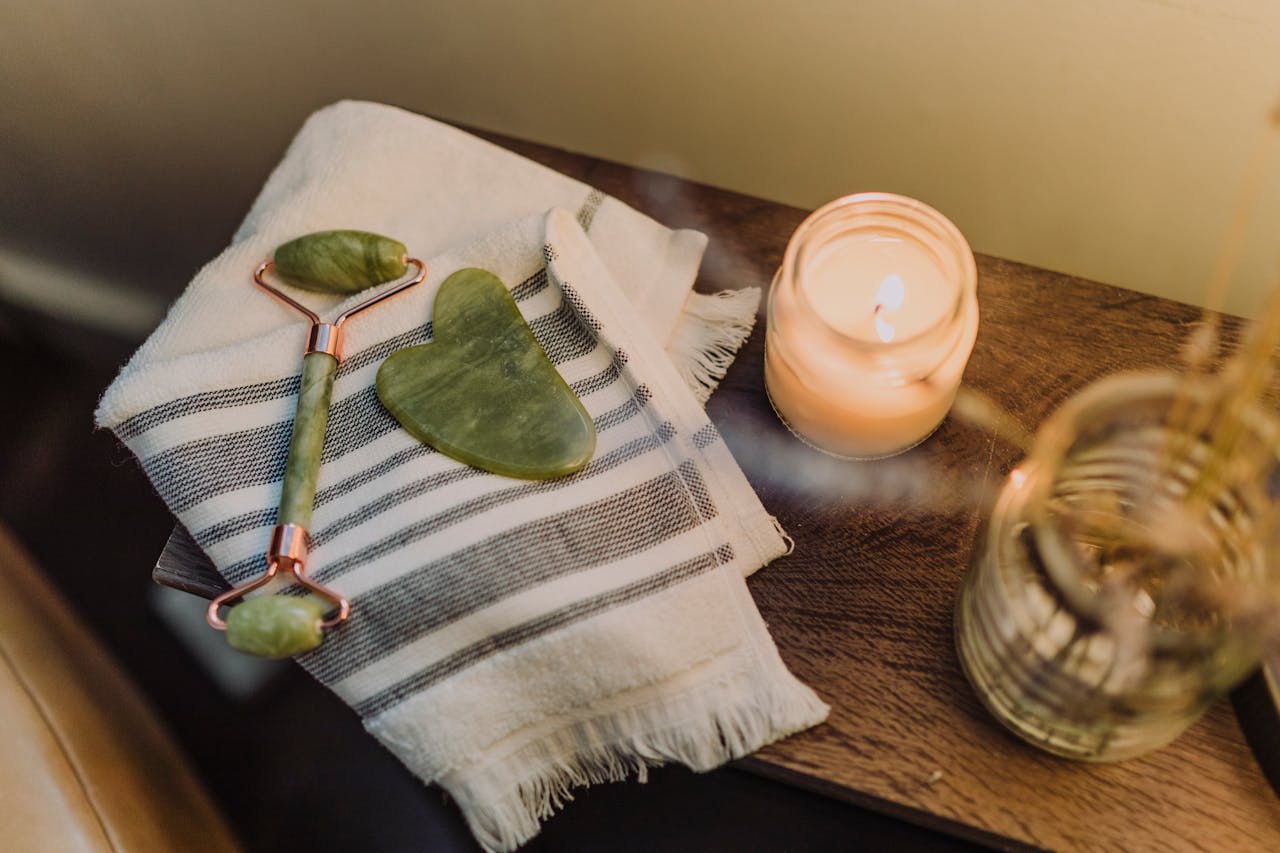 experience-img Calming spa setup featuring a jade roller, gua sha stone, and candle for relaxation and skincare.