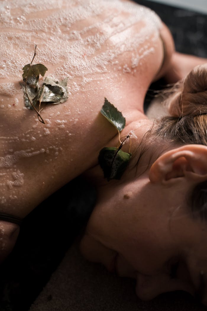 our-journey-01 Close-up of a woman enjoying a relaxing spa treatment with natural leaves and exfoliation.